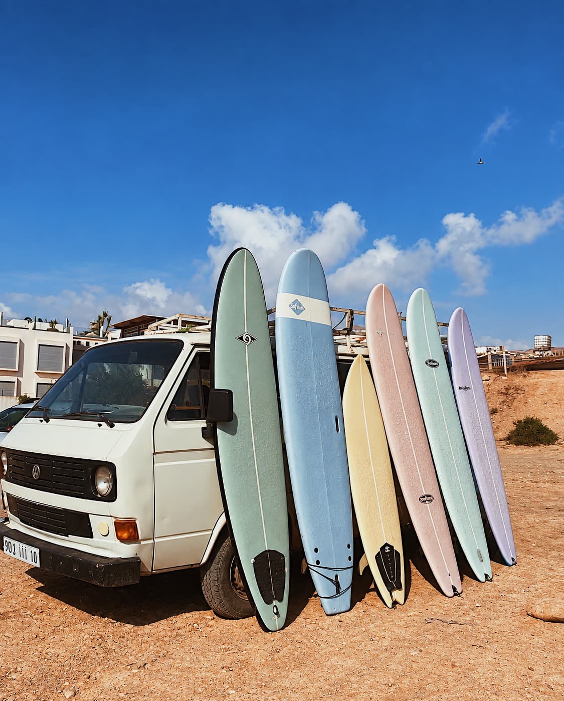 A row of colourful surfboards leaning against a vintage van on a sunny beach
