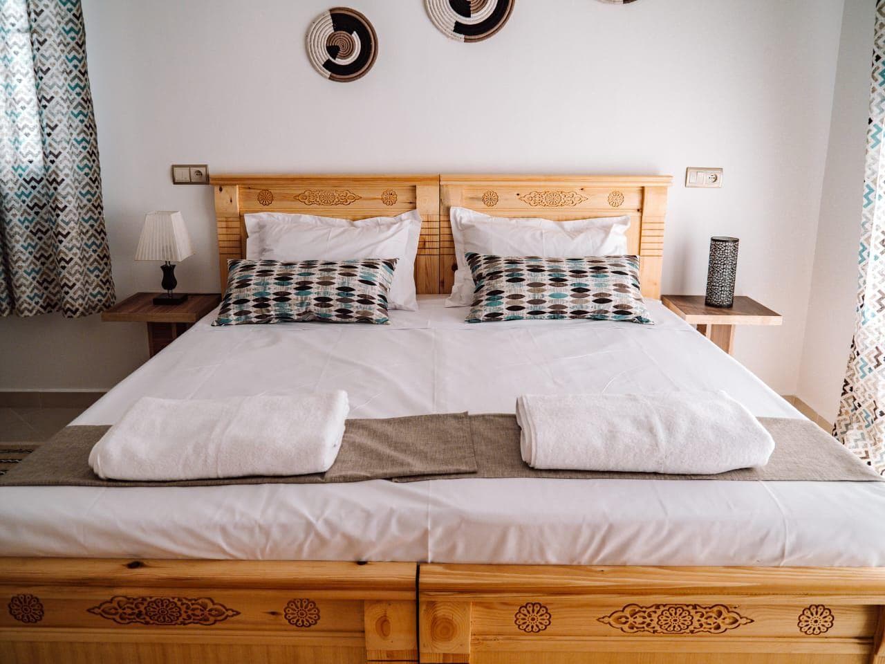 A styled bedroom with a carved wooden bed and a woven pendant light